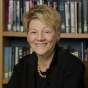 Person smiling in front of a bookshelf wearing a black top and necklace